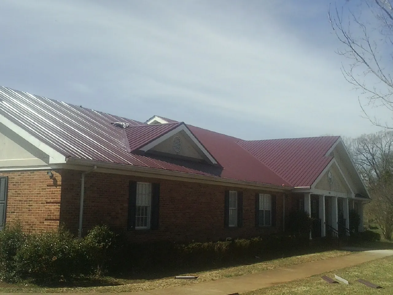 Red metal roof with gabled entries on a long brick building, from a Hail Damage Roof Repair job in Matawan
