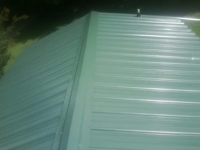 New green metal panels meeting at the ridge of a roof — Flat Roof Repair work by our crew in Matawan