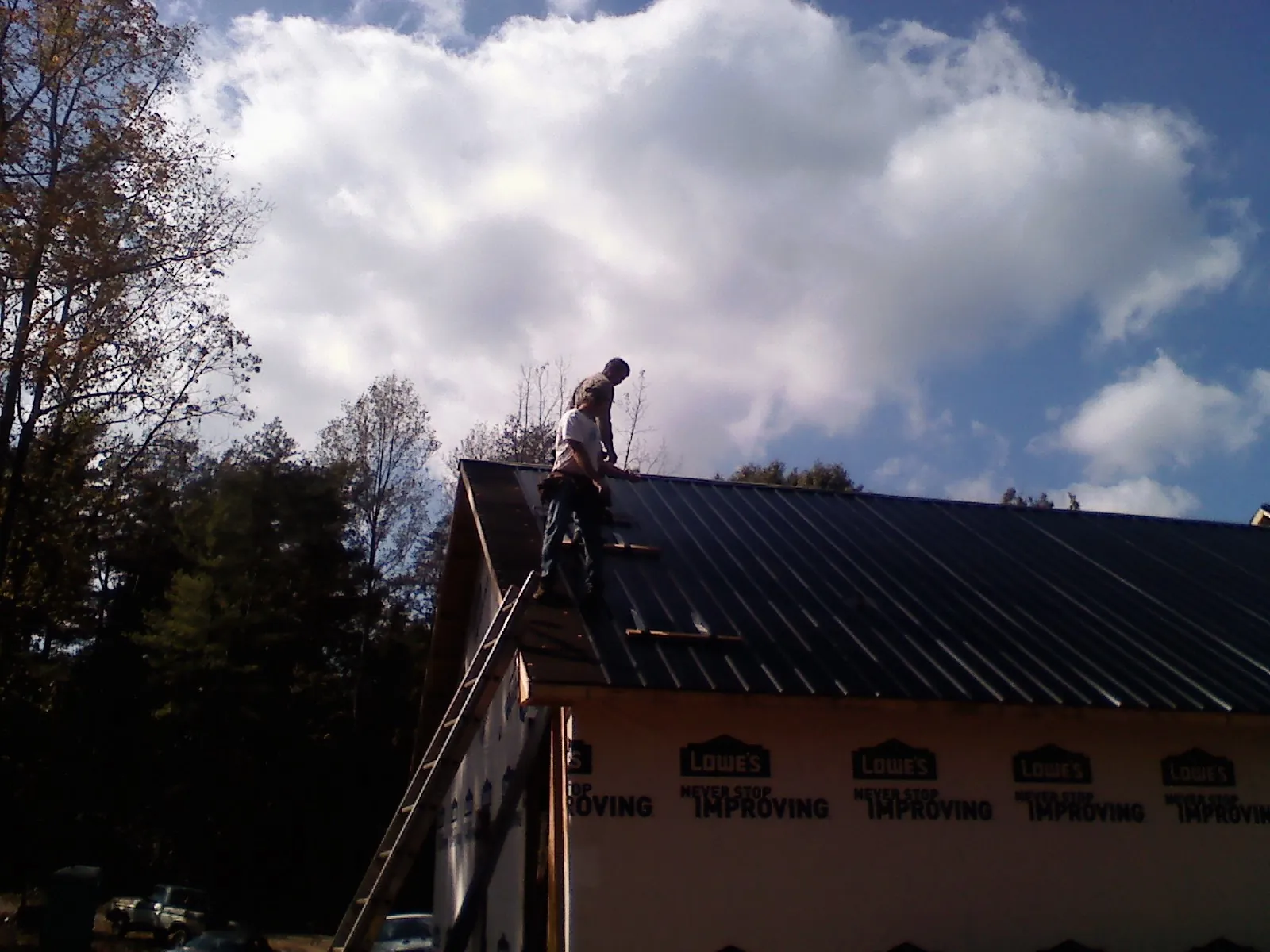 Roofer fastening dark metal panels high against a cloudy sky, from a Roof Inspection job in Matawan