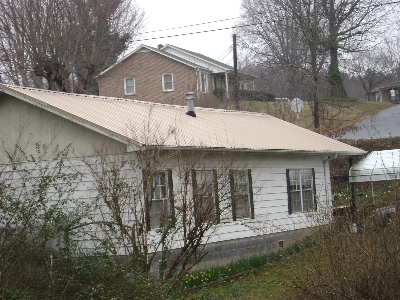 Tan metal roof on a white sided house set into a hillside — Commercial Roofing by Roofing Brothers in Matawan